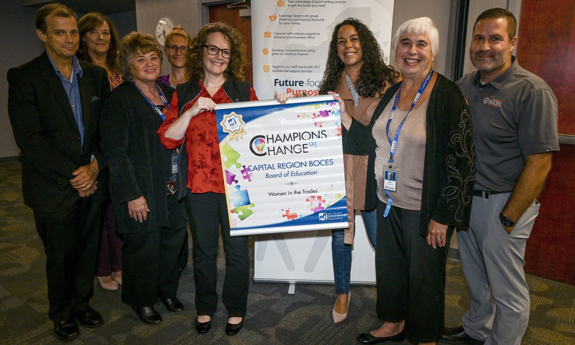 A group of BOCES employees line up holding a banner that reads "Champions of Change."