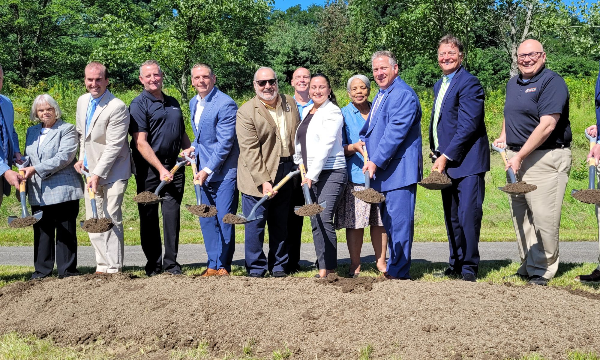 A group of legislators and community leaders stand in line with shovels in hand during a groundbreaking ceremony.