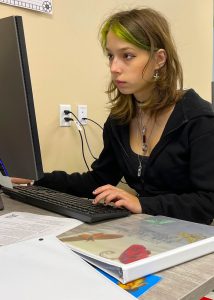 A female student in a black hoodie types on her computer keyboard while looking at her screen.