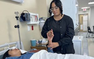 A student in dark clothing looks over a patient lying in a simulated hospital bed at BOCES.