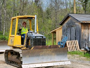 A student in a reflective safety vest sits behind the steering wheel of a bulldozer.