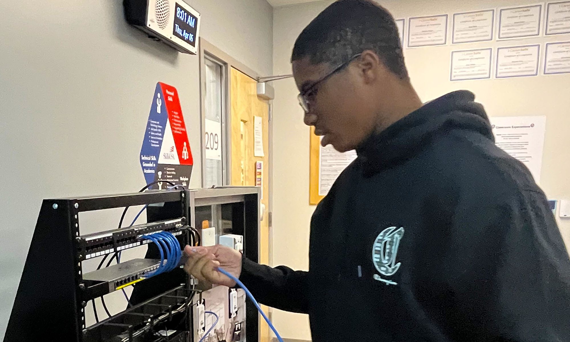 A student in a navy blue hoodie works on a cable networking exercise.