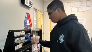 A student in a navy blue hoodie works on a cable networking exercise.