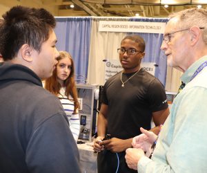 Three students circle around a teacher in the midst of conversation.