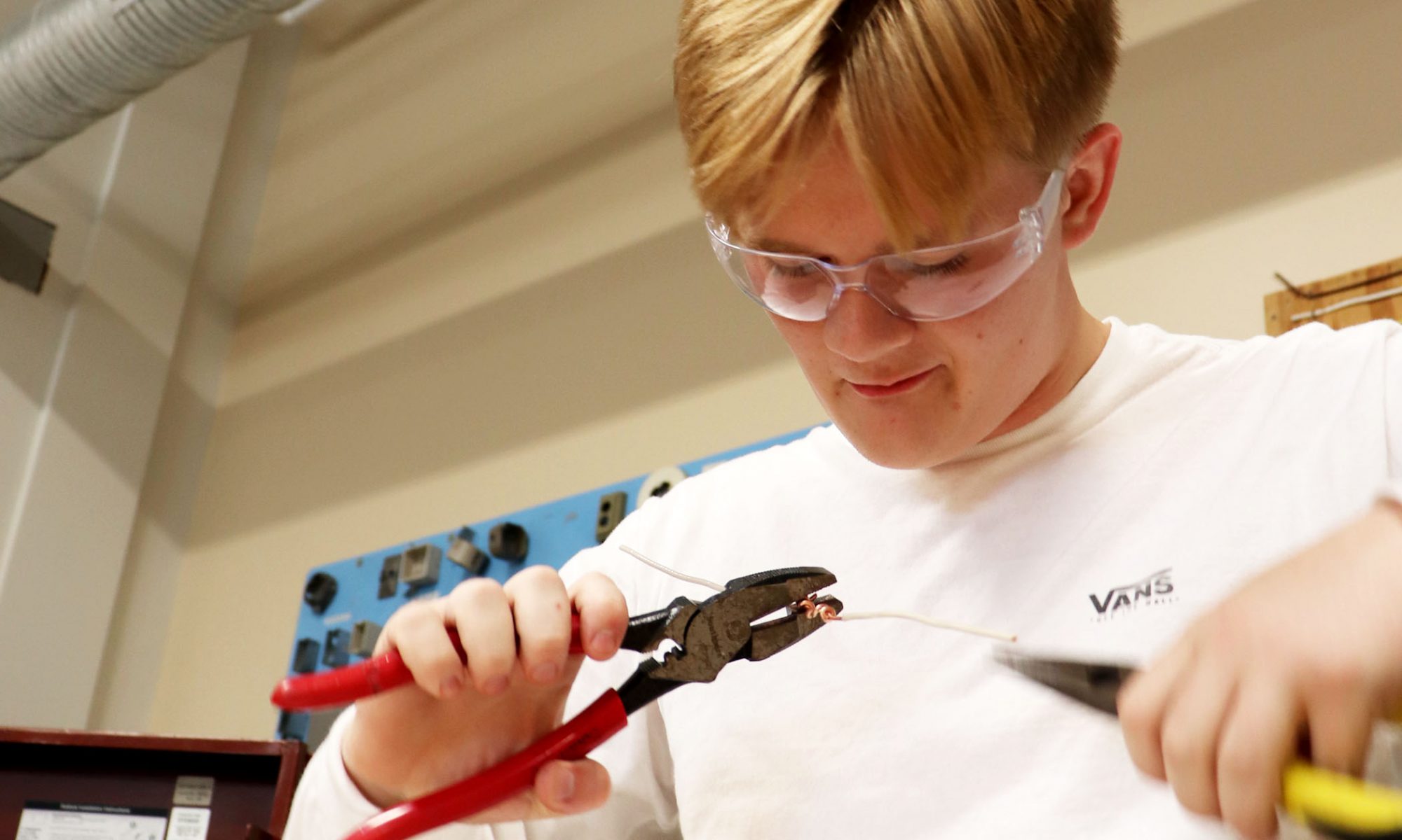 A student handles an electrical wire with a set of pliers in each hand.