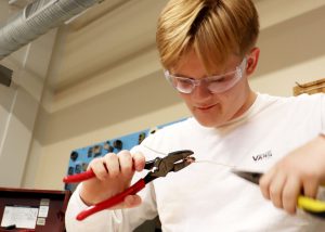 A student handles an electrical wire with a set of pliers in each hand.