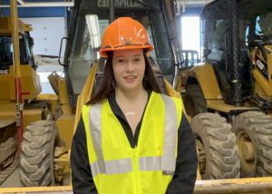 A female student wears a yellow safety vest and an orange hardhat.