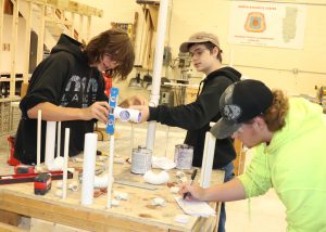 Three students work together on a pipe fixture, with one student holding a level to judge whether to joint is level.