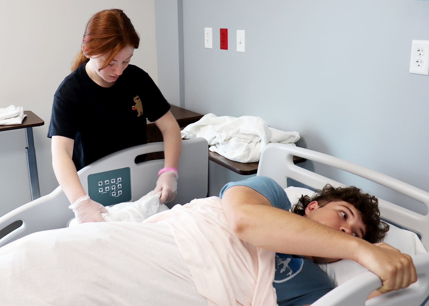 A health career program student tends to a patient in bed.