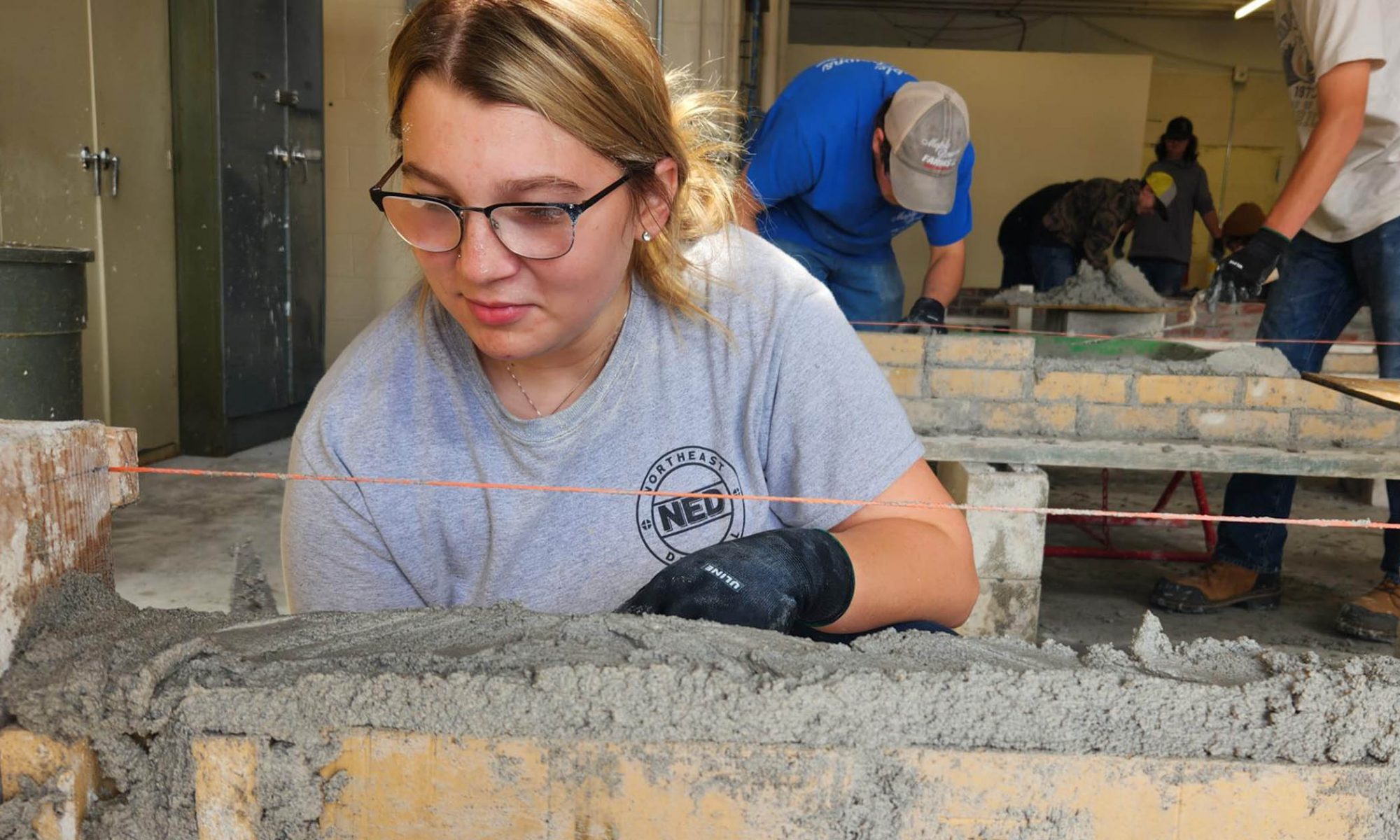 a female masonry student eyes her work and keeps it level