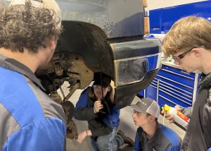 Four students look at the front end of a car from various angles as they work to repair the unseen problem.
