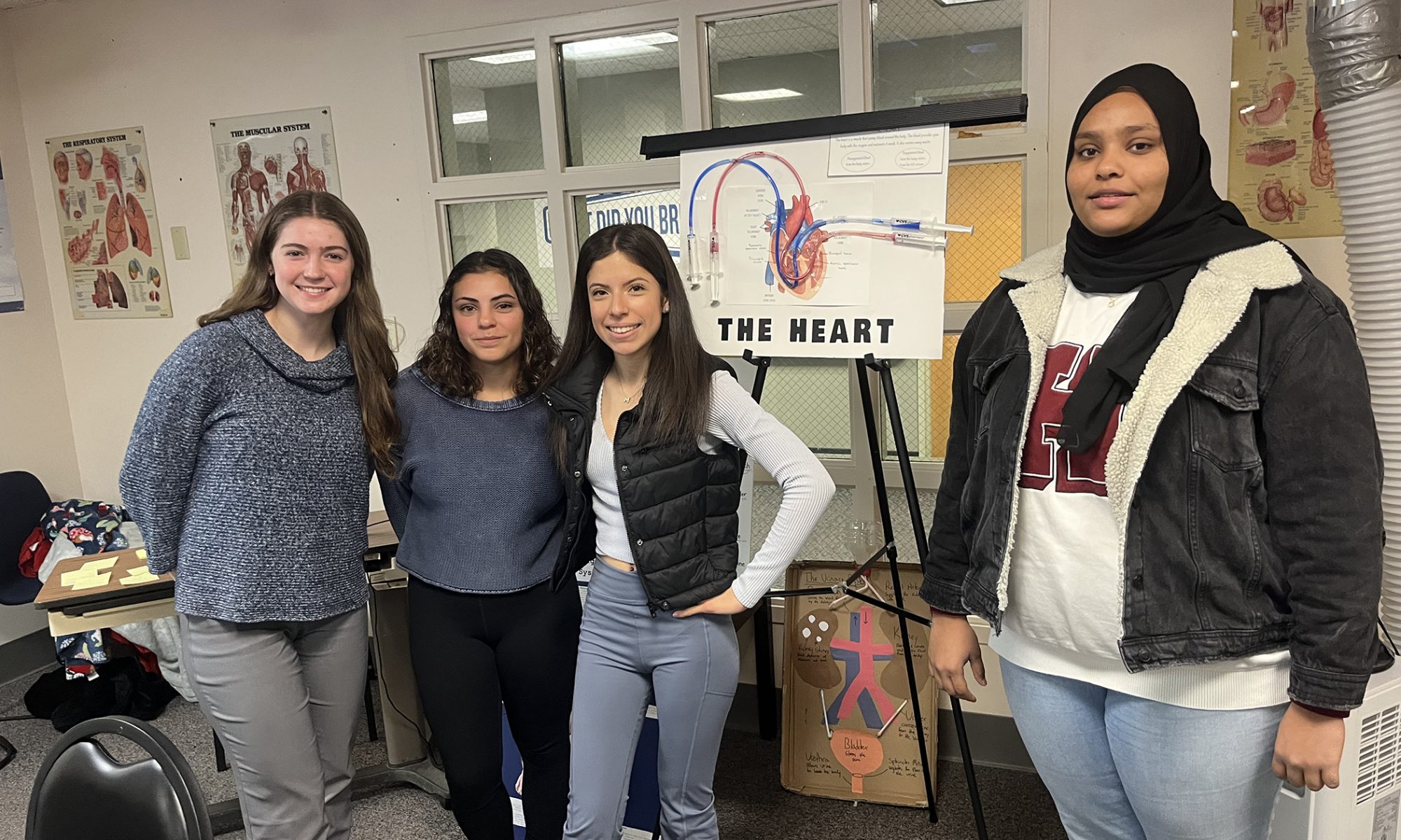 Four students stand in front of a diagram of the human heart as they pose for the photo.