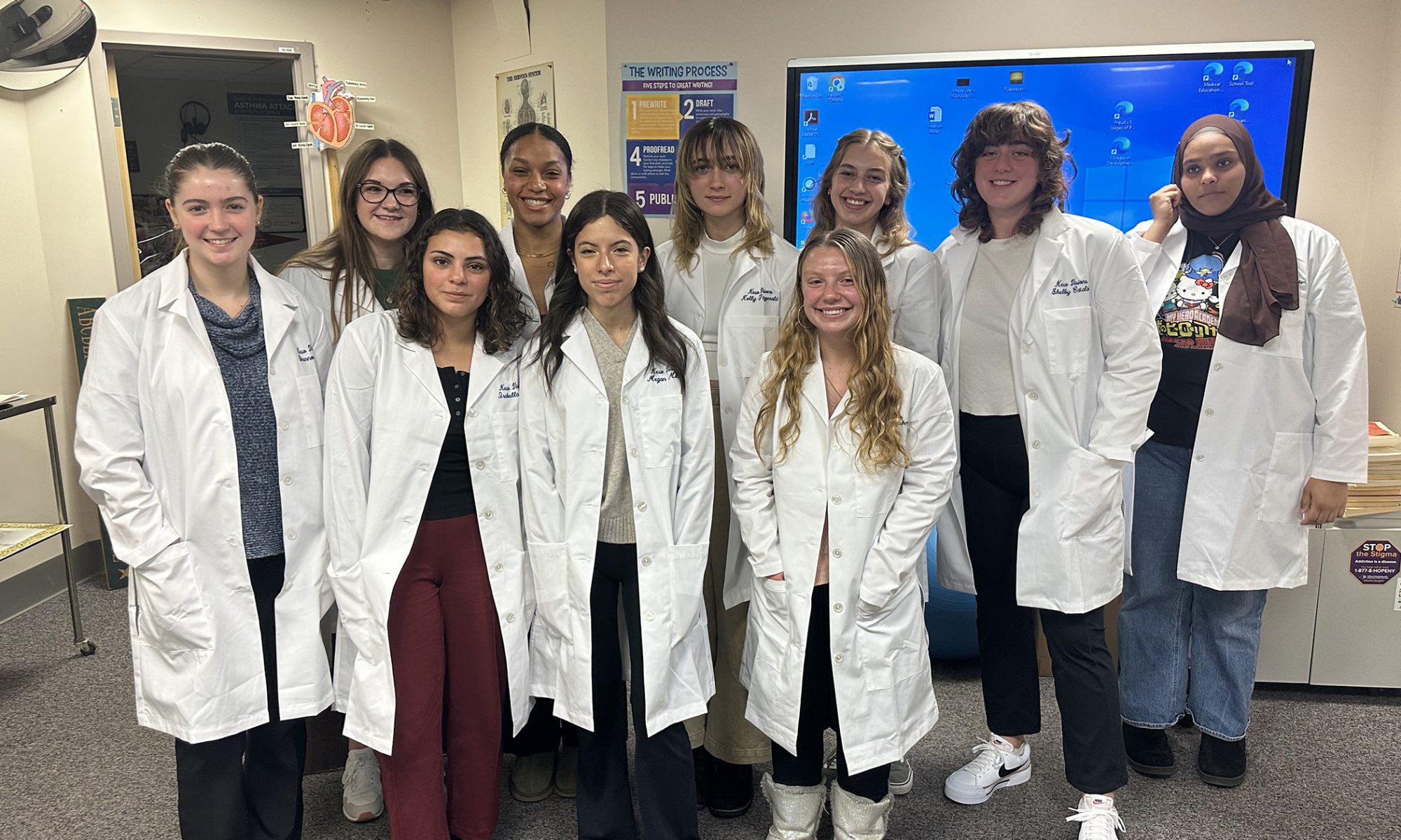 Several individuals stand in two rows as they pose in their white labcoats.