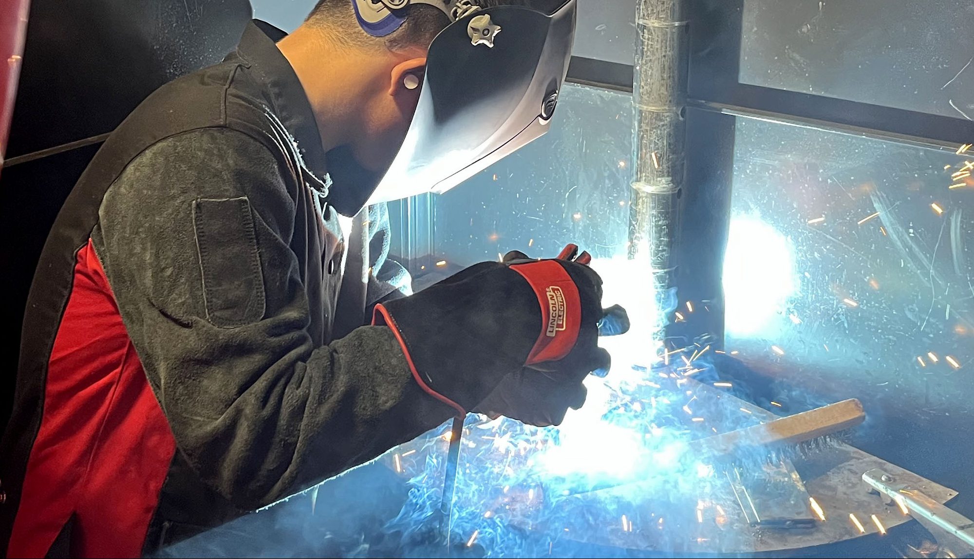 A student in a welder's and safety gloves goes to work with his torch.