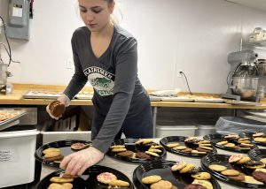A student stands over several dishes of holiday cookies as she arranges them in a neat display.