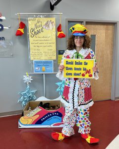 A woman in clown's outfit holds a sign that reads, "Should Smiles the Clown donate his clown shows?"