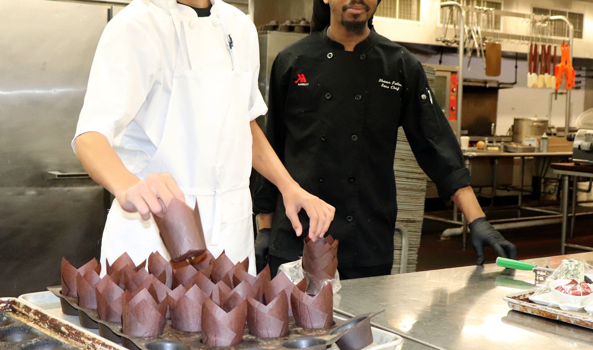 A chef and his student prepare a dish from inside the kitchen.