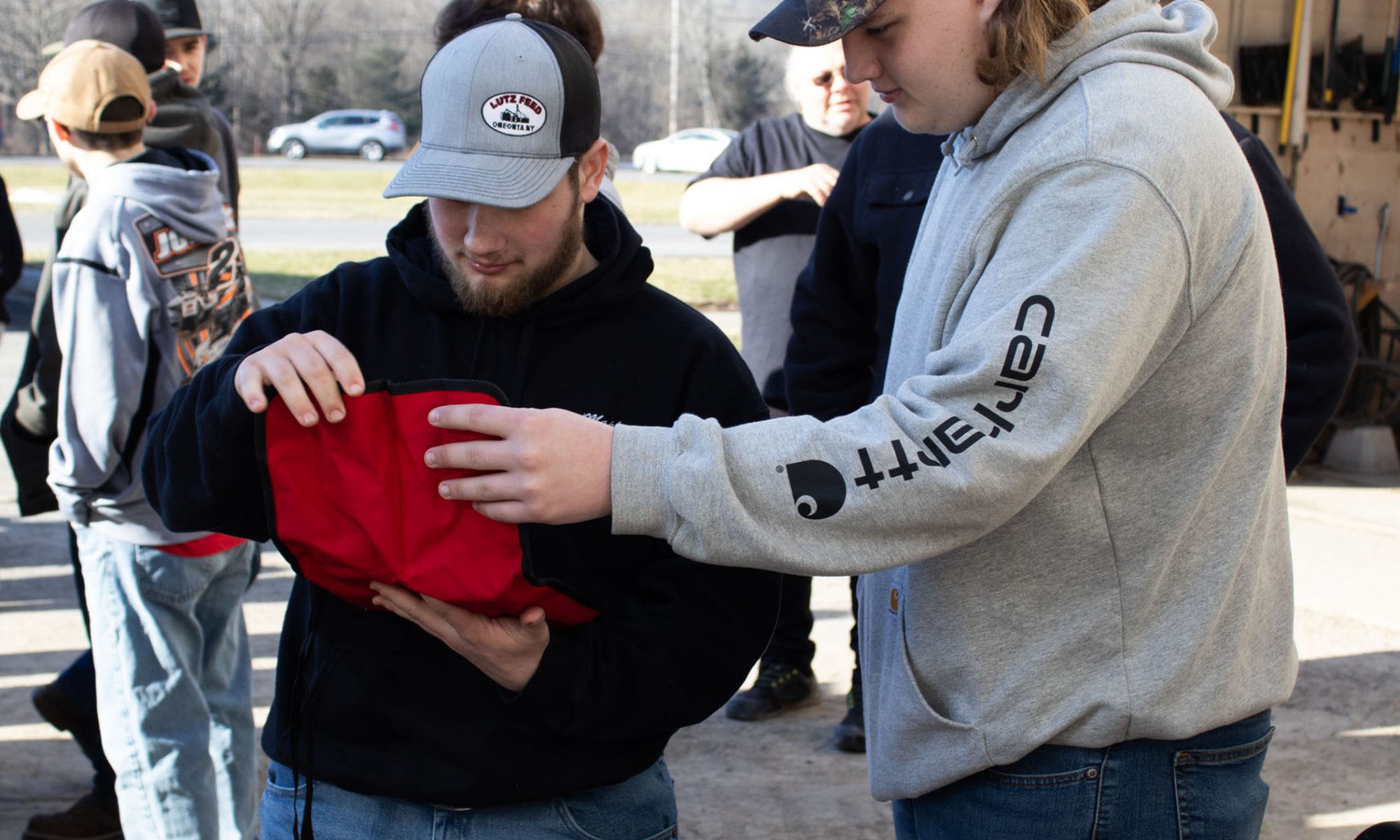 Two students in baseball caps, one in a blue hoodie and another in a grey one, look at the contents inside of a red canvas bag during an outside exercise in the Heavy Equipment program.