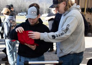 Two students in baseball caps, one in a blue hoodie and another in a grey one, look at the contents inside of a red canvas bag during an outside exercise in the Heavy Equipment program.