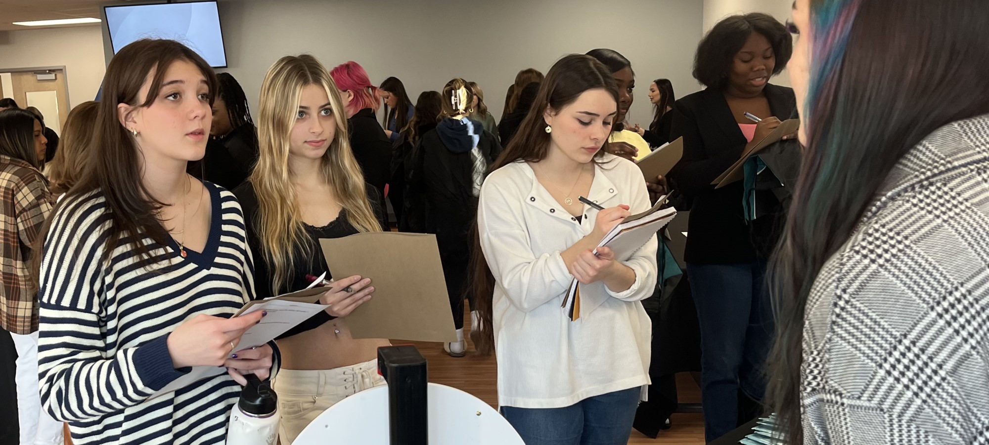 Three prospective cosmetology students ask questions and take notes during an open house event.