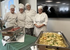 Four culinary students stands behind a display of food ready to serve.