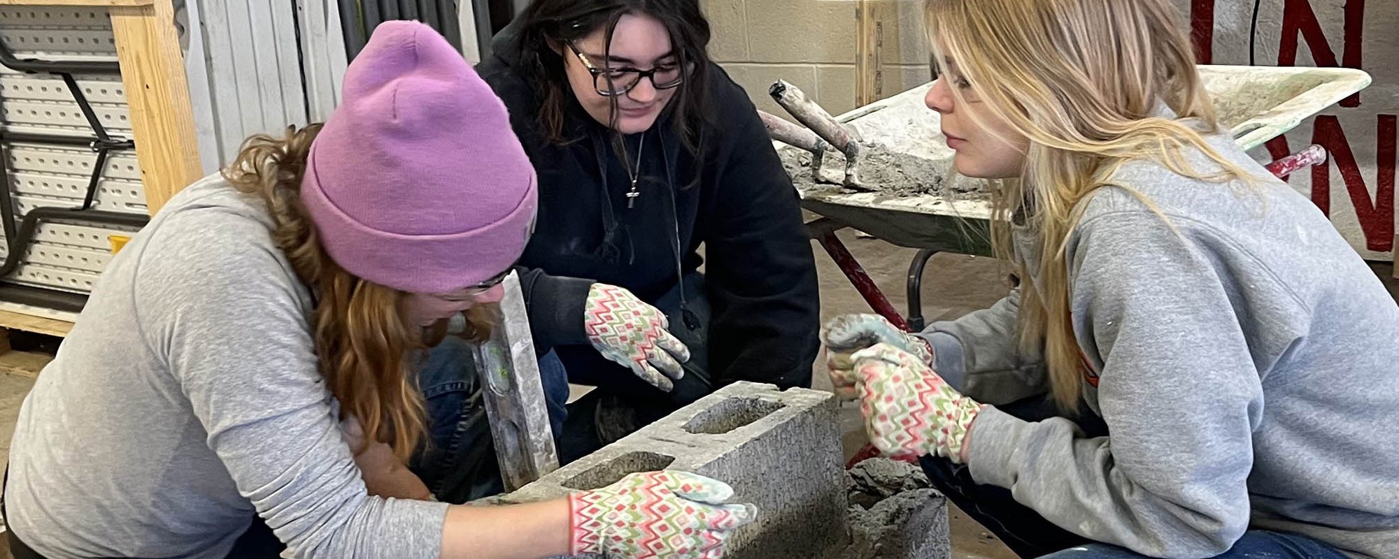 Three students work together to lay a brick down.