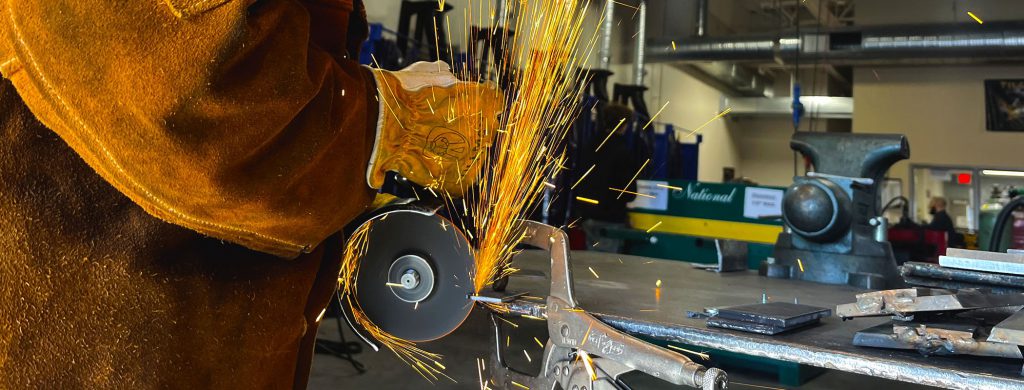 A welder's gloved hands are showered by yellow and orange sparks in the midst of a project.