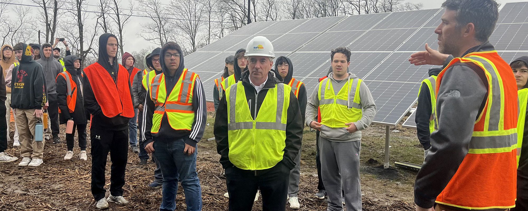 A crowd gathers in front of a solar array for a presentation.