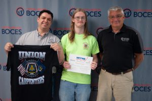 A student stands to pose for a picture  with his Signing Day certificate in hand while flanked by representatives from his future employer.