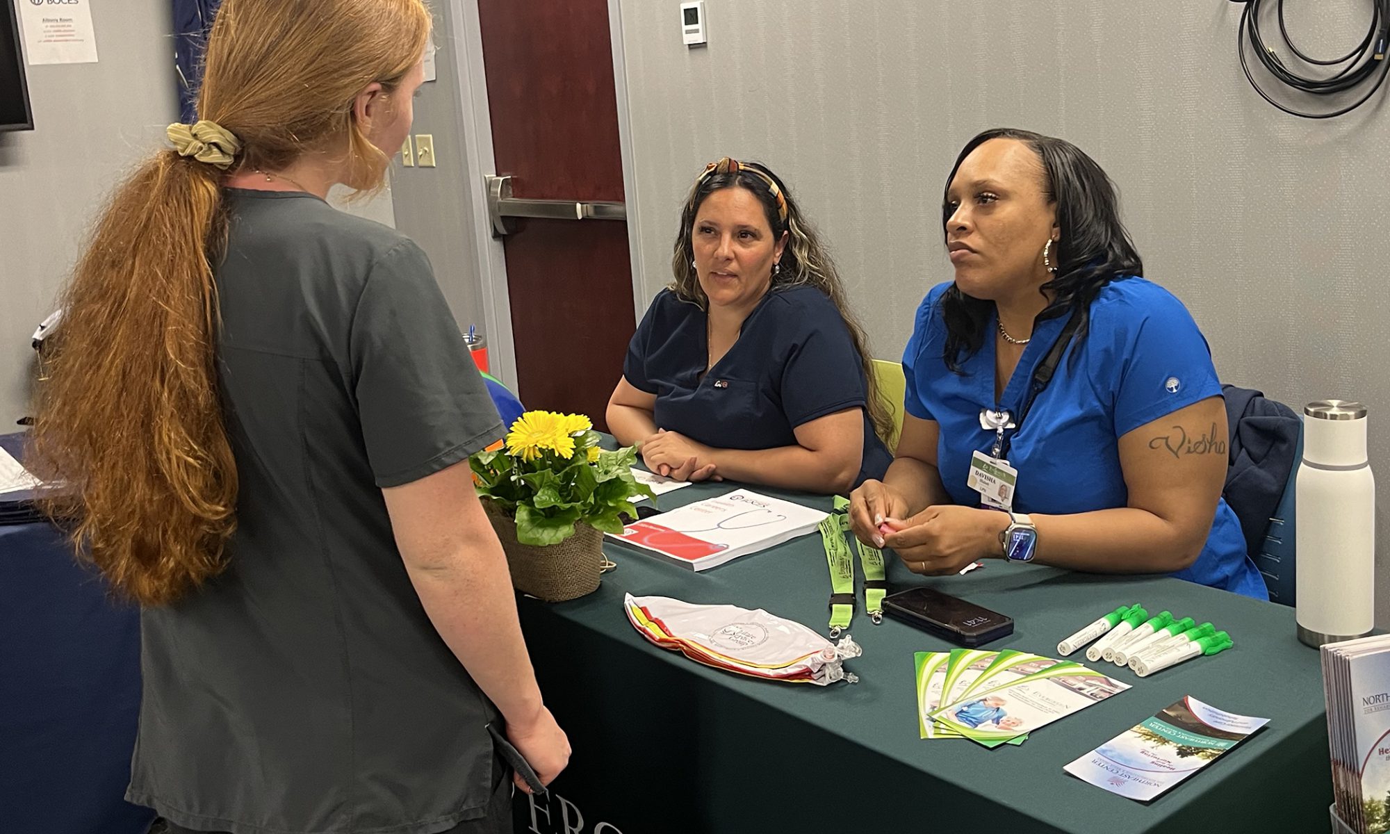A prospective employee stands in front of a table where two employers sit and attentively listen.