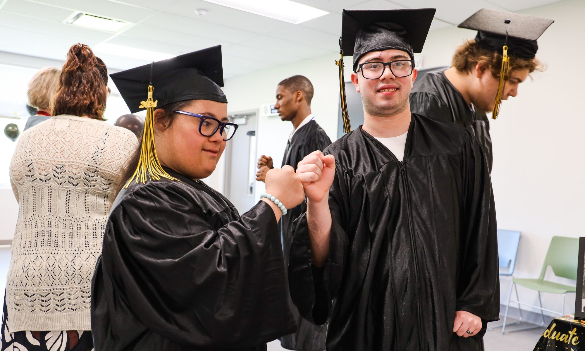 Two students in cap and gown fist bump to celebrate the coming graduation ceremony.