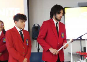 students in matching blazer stand behind a table with candles