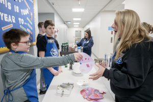 Airline Academy student Carter Parker hands speech therapist Heather Hopke a kindness note at their Kindness Cart at Airline Academy
