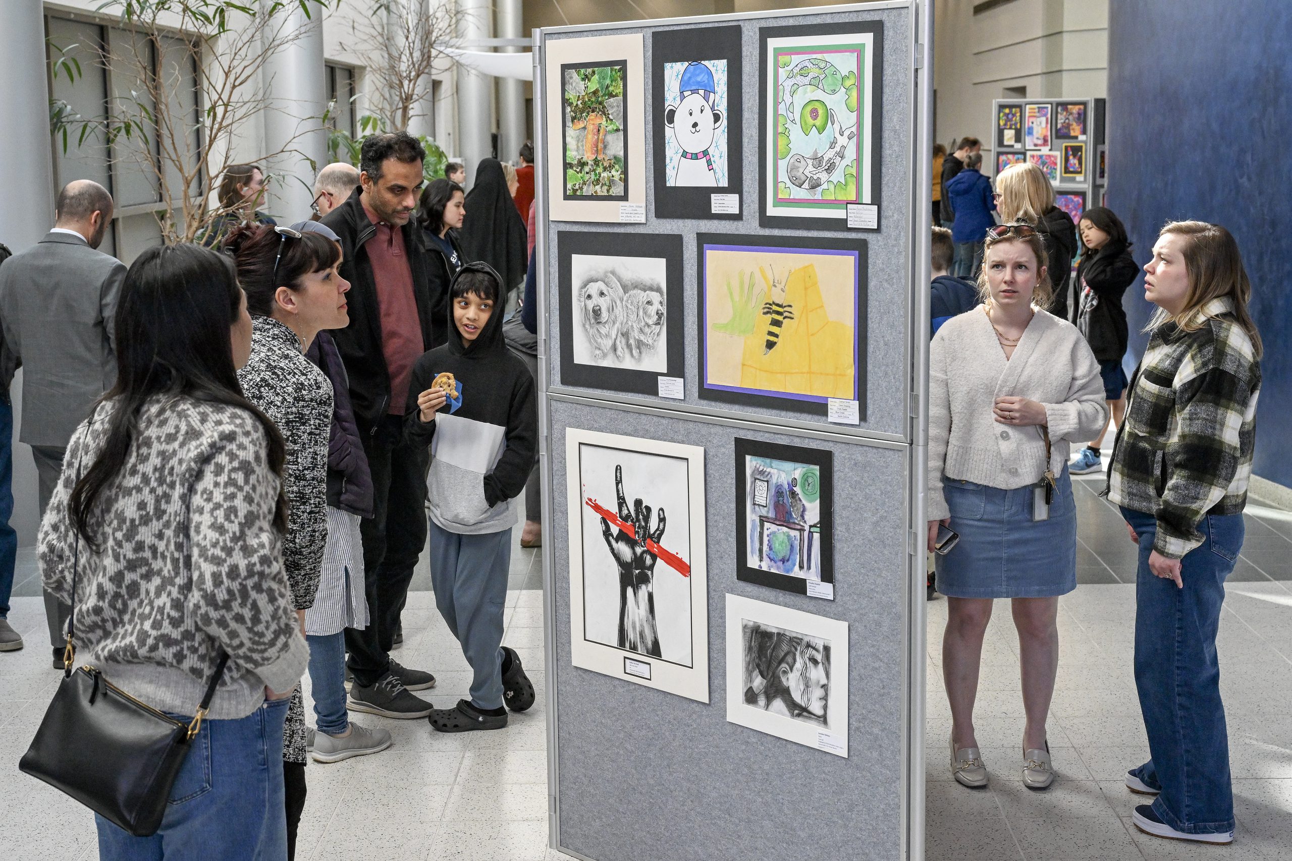 People are at an art show looking at student artwork that is hanging on the walls