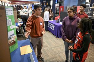 A student speaks in from of a display while two other students listen.