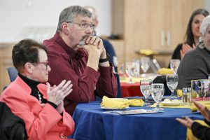A meeting participant claps his hands as he listens at a table.