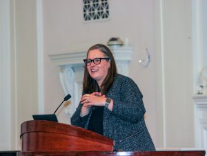A speaker is standing at a podium, smiling
