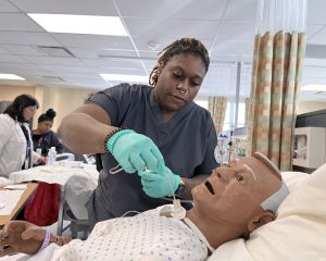 A student inserts a suction tube into a mannauin