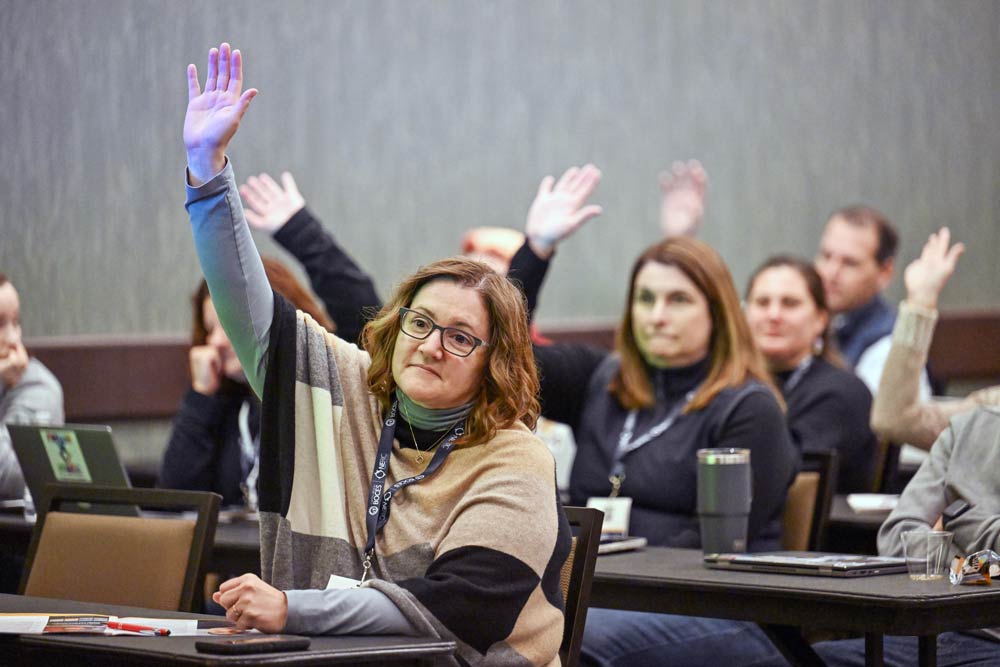 Several adult students seated at their desks raising their hand