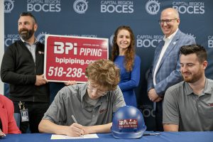 Student signs a letter of intent as dignitaries looks on