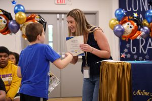 Teacher shakes student's hand as she presents him with a certificate. 
