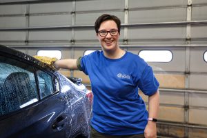 SELFI Program student Elizabeth Lorini is smiling for the camera as she washes a car in the garage at Metro Ford in Schenectady, New York.