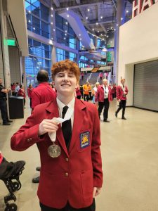A student in s red coat holds a medal up