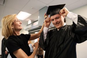 A Maywood Academy social worker is pictured helping a graduate adjustment his cap and gown.