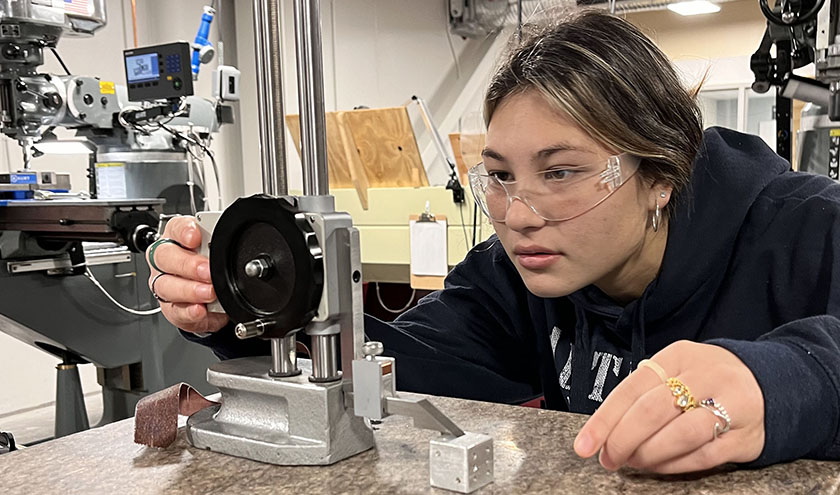 Two health careers students, one wearing a protective mask on her mouth, work on a project.