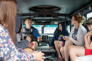 Students and their teacher sit with a first responder in the back of an emergency vehicle. 