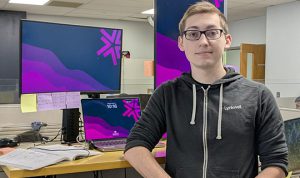 A man with glasses and a Lynkwell hoodie stands in front of computer screens