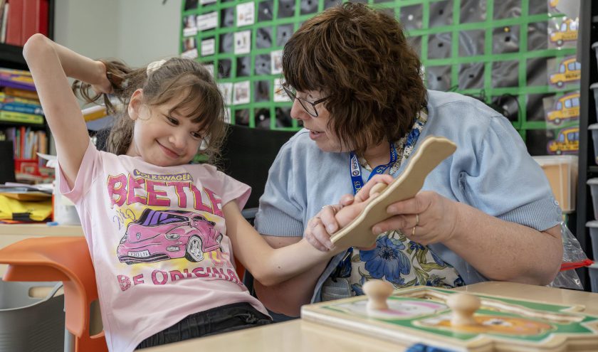 Two smiling teachers hand a student wearing a graduation cap and gown her diploma.