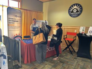 Two people speak to a person who is manning a table at a conference