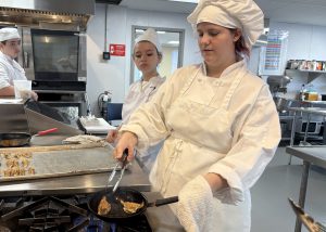 Lacey cooks as a student looks on